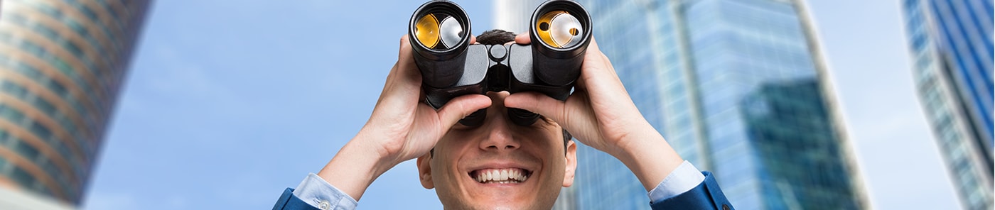 Businessman looking through binoculars among office towers
