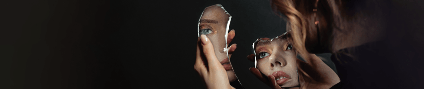 Woman studying her reflection in pieces of a broken mirror