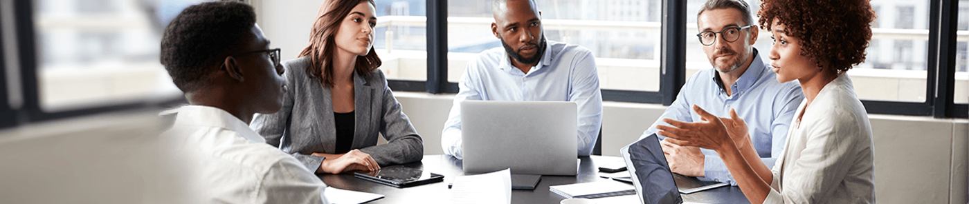 Colleagues in discussion around a meeting table with laptops